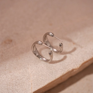 Gros plan de boucles d'oreilles argentées minimalistes sur un fond de pierre beige