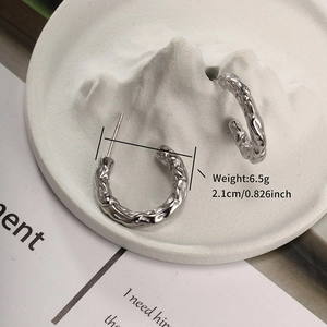 Detail of silver C-shape earrings with lava texture on white decorative stone stand