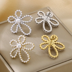Macro detail of floral pearl stud earrings in gold and silver finish on metallic tray