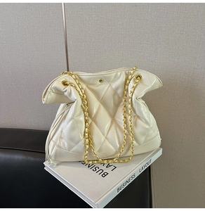 Close-up of white quilted bucket bag with gold chain strap resting on books