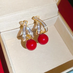 Detail of cross-shaped gold earrings with zircon crystals and a red pearl pendant