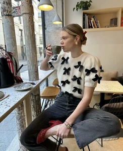 Détail du pull en tricot blanc à manches courtes avec plusieurs nœuds noirs décoratifs