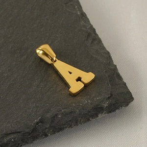 Macro shot of gold stainless steel letter A pendant on textured dark stone surface