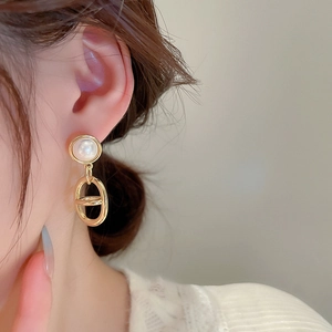 Detail of gold dangle earring with a white pearl and hollow geometric link design