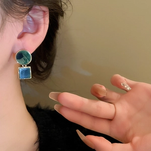 Close-up of geometric acetate earrings in green and blue on model for a trendy style