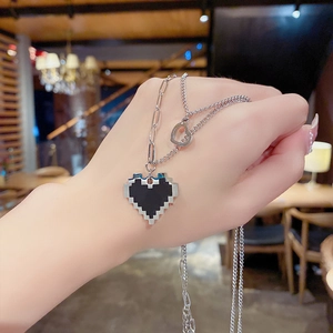 Détail montrant un collier double rang argenté avec pendentif cœur noir porté à la main