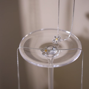 Elegant silver daisy pendant necklace set with yellow accents on a wine glass