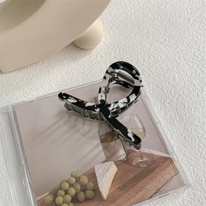 Close-up of a marbled acetate hair claw clip with black and white texture on an artistic box