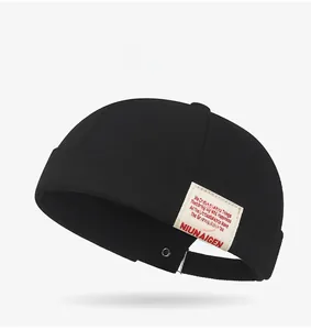 Detail of a black cotton docker hat featuring a white woven label and adjustable buckle strap