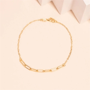 Detail of gold paperclip and cross chain bracelet with a lobster clasp on beige background