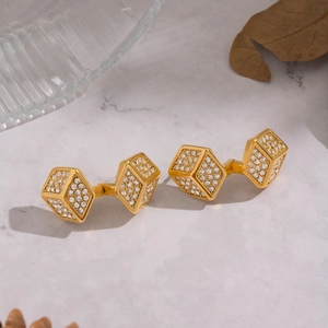 Golden cubic dice earrings with white crystals on a marble surface background