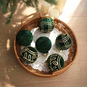 Detailed view of six dark green velvet Christmas balls with gold glitter patterns in a tray
