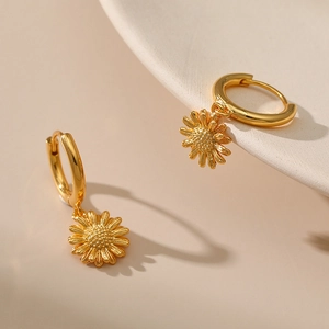 Close-up of gold sunflower dangle earrings on a ceramic tray with soft shadows