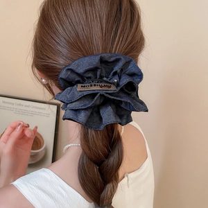 Detailed view of deep blue denim hair scrunchie with label on model braided hair