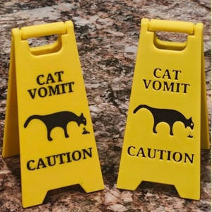 Macro shot of two yellow plastic caution signs featuring black cat vomit warning text