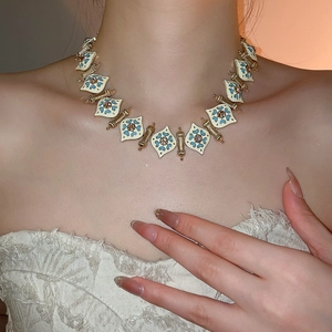 Close-up of vintage gold necklace with blue and white enamel diamond patterns on a model
