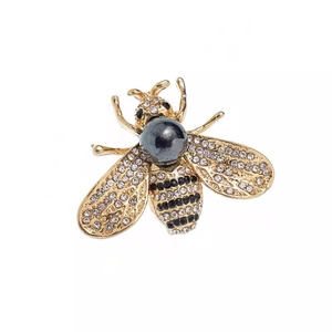 Luxury gold bee brooch with rhinestones and grey pearl accent on a white background