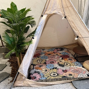 Bohemian floral camping blanket with tassels inside a cozy lit outdoor tent setup