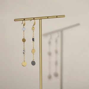 Macro shot of long bicolor tassels earrings with gold and silver round discs on metal stand
