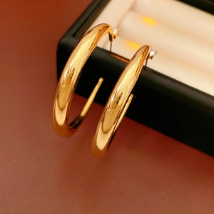 Close-up of gold C-shaped hoop earrings with zircon studs on dark red leather texture