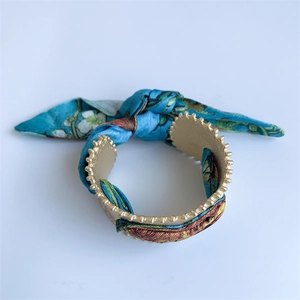 Detail of matte gold open cuff bracelet with blue floral silk scarf wrap and textured edges