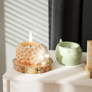 Detail of lit hedgehog and bird ceramic candles on white surface with soft shadows