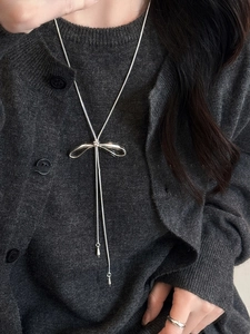 Close-up of a silver bow necklace with snake chain texture on a model's grey cardigan
