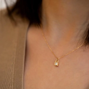 Close-up of a gold-plated key lock pendant necklace with a round crystal on a model