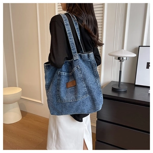 Detail of blue washed denim tote bag showing the front pocket and brown leather brand label