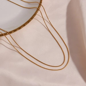 Detail of minimalist 18K gold plated double layer snake chain on white ceramic plate