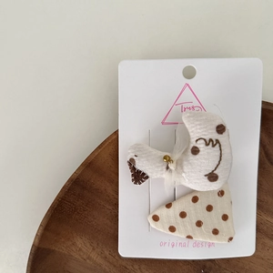 Close-up of handmade beige polka dot fabric hair clips with a bird and triangle design