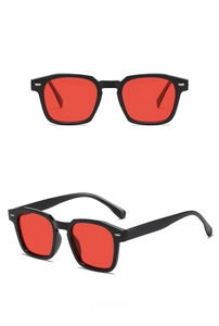 Detalle de gafas cuadradas con montura negra, lentes rojas y remaches metálicos