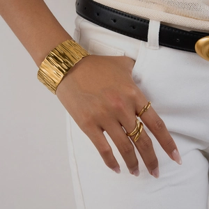 Detail of 18K gold plated wide cuff bracelet with ripple texture and minimalist rings