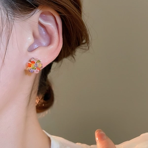 Close-up of colorful crystal flower stud earrings on model ear featuring 3D floral design