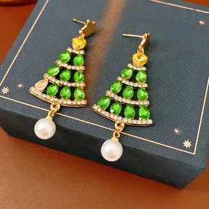 Close-up of golden Christmas tree earrings with green crystals and pearl pendant