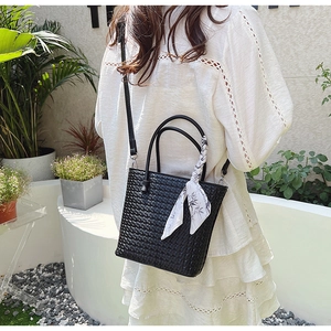 Close-up of woven bucket bag featuring a floral silk scarf and leather top handle