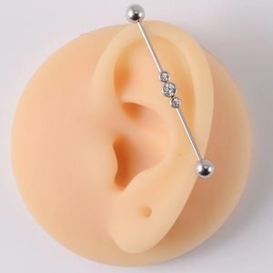 Detailed view of silver industrial barbell with three clear gems on silicone ear model