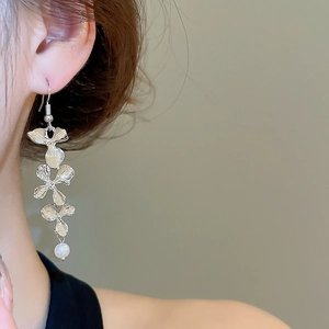 Detail view of silver metal flower drop earrings with pearl tassels on a female model