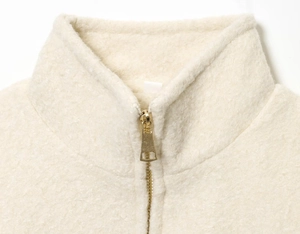 Close-up of stand-up collar and gold metal zipper on cream-colored sherpa jacket