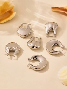 Détail de six boucles d'oreilles argentées polies sur fond de plage avec coquillage d'été