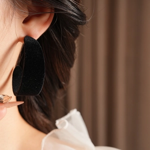 Detail of model wearing a black flocked C-shaped earring with soft velvet texture
