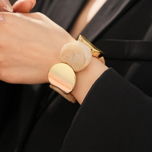 Close-up of a wide elastic bracelet with gold metal and marble resin links on a sleeve