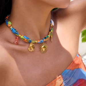 Detail of bohemian gold charms and red beads on a colorful fabric necklace on skin