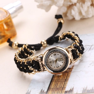 Detail of a women's gold quartz watch with a black braided strap and sparkling rhinestone bezel