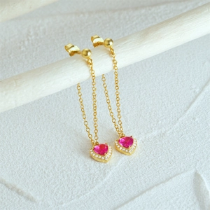 Detail of gold dangle earring with pink heart zircon pendant on white branch
