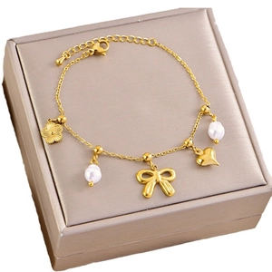 Gouden armband met strik, hart, parels en schelphangers op een sieradendoosje