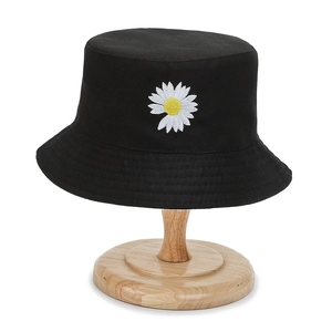 Minimalist black cotton bucket hat with white daisy embroidery on a wooden stand
