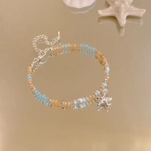 Detail eines Perlenarmbands mit Seesternanhänger und dekorativen Meeresmuscheln