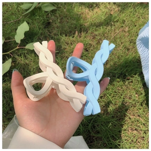 Blue and white matte braided hair claws held over a natural green grass background