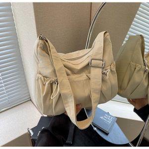 Detail of beige nylon crossbody bag featuring side drawstring pleats and adjustable strap
